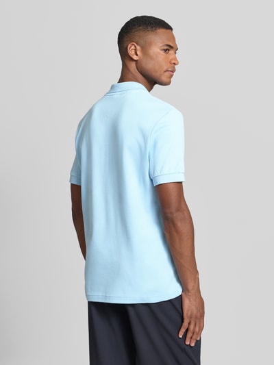 Męski model nosi Regular Fit Poloshirt aus reiner Baumwolle von Lacoste, efekt: jednolity kolor, detal z logo marki, kołnierzyk polo, dekolt w serek, krótki rękaw, prążkowane zakończenie rękawa, wykończenie z bocznymi rozcięciami, asymetryczny dół, materiał: bawełna, całkowity widok z tyłu.