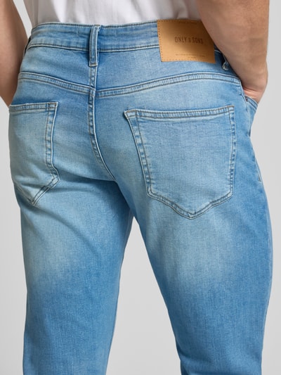 Männermodel trägt Slim Fit Jeans aus Baumwoll-Mix Modell 'LOOM' von Only & Sons, hellblaue Denim, Label Patch, Ganzkörperansicht Rückansicht.
