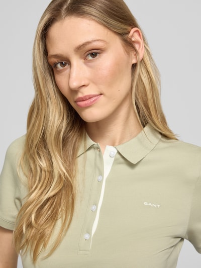 Frauenmodel trägt Slim Fit Poloshirt mit Label-Stitching von Gant aus Baumwoll-Elasthan-Mix, Knopfleiste, Rückenlänge 59 cm, Nahaufnahme Oberkörper.