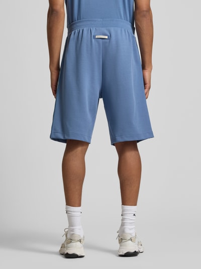 Männermodel trägt Sweatshorts mit Label-Details und Eingrifftaschen von EA7 Emporio Armani in Blau, Baumwoll-Mix, Relaxed-Fit, Ganzkörperansicht Rückansicht. Bundweite bei Größe M 47 cm, Innenbeinlänge 29 cm.