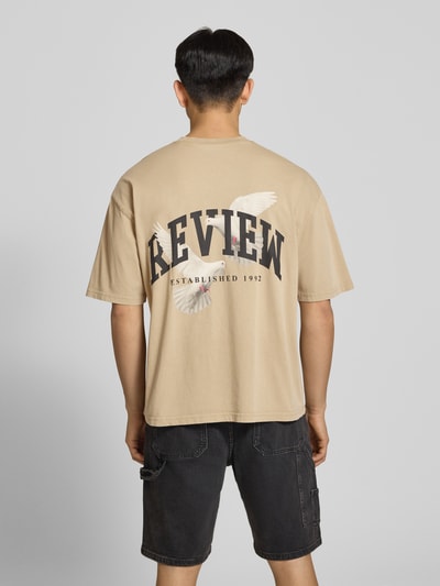 Männermodel trägt T-Shirt mit Logo- und Motiv-Print von REVIEW in Beige, Reine Baumwolle, Loose-Fit, Ganzkörperansicht Rückansicht.