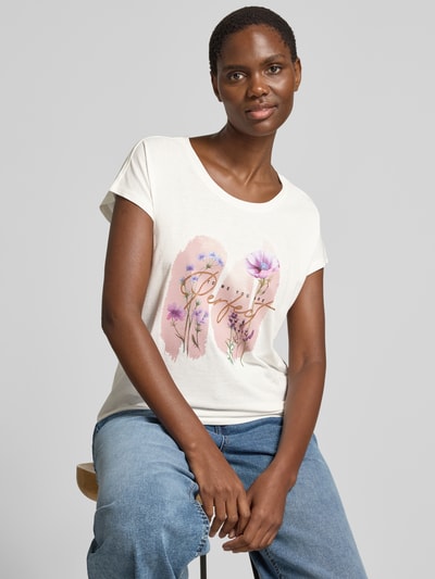 Frauenmodel trägt T-Shirt mit Motiv- und Statement-Print von Christian Berg Woman, Baumwoll-Viskose-Mix, Regular-Fit, Rundhalsausschnitt, Damen T-Shirt, Rückenlänge bei Größe S 56 cm, helle Farben, florales Muster, schlichte Struktur, Nahaufnahme Oberkörper.