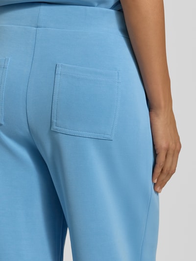 Frauenmodel trägt Wide Leg Sweatpants aus Modal-Mix von Rich & Royal in Hellblau, glatte Textur, Gesäßtaschen, Detailaufnahme Rückansicht. Damen Sweatpants von Rich & Royal, Modal-Mix, Wide Leg, elastischer Bund, Bundfalten, seitliche Eingrifftaschen, Gesäßtaschen, Innenbeinlänge bei Größe S: 64 cm.