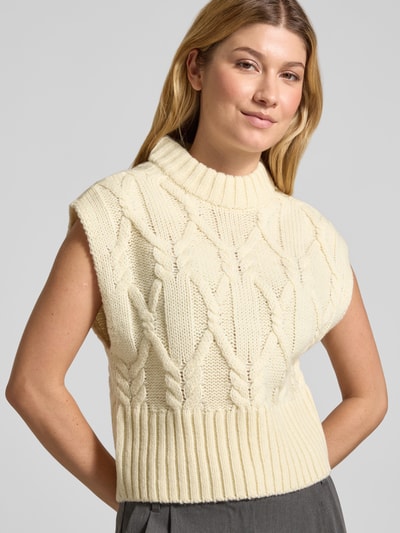 Frauenmodel trägt Strickpullunder aus Woll-Mix mit Stehkragen Modell 'MAGLE' von Cph Muse, cremefarben, Zopfmuster, Nahaufnahme Oberkörper. Rückenlänge bei Größe S: 50 cm, Regular Fit.