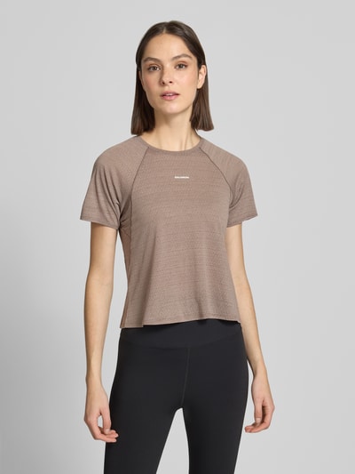 Frauenmodel trägt Cropped Fit T-Shirt mit Logo-Print von Salomon, braun, Rundhalsausschnitt, kurzärmelig, Ganzkörperansicht von vorne.