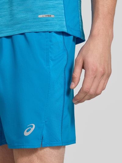 Męski model nosi Regular Fit Shorts mit integriertem Slip Modell 'Core' od ASICS TIGER, niebieskie, nadruk z logo, elastyczny pas, Szerokość w rozmiarze M: 38 cm, Długość wewnętrzna nogawki w rozmiarze M: 17 cm, zbliżenie na górną część nóg.