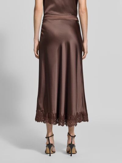 Vrouwenmodel draagt Midirok uit satijn met kanten rand van Christian Berg Woman Selection, elastische materiaalmix, nauwsluitende pasvorm, maat 36 bandwijdte 38 cm, totale lengte 90 cm, bruine kleur, gladde textuur met kant, geheelopname achteraan.
