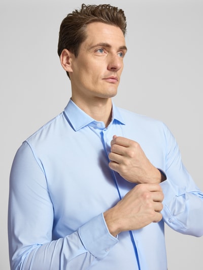 Mężczyzna nosi Slim Fit Businesshemd mit Knopfleiste od CRUNA, materiał z domieszką stretchu, krój slim fit, kołnierz kent, zapięcie na guziki, długość tyłu w rozmiarze 50: 65 cm, szerokość w rozmiarze 50: 43 cm, długość rękawa w rozmiarze 50: 65 cm, jasnoniebieski kolor, gładka tekstura, zbliżenie na górną część ciała