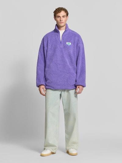 Männermodel trägt Oversized Pullover mit Stehkragen Modell 'HOKTOWN' von American Vintage, Kunstfell, Logo-Patch, Ganzkörperansicht von vorne.