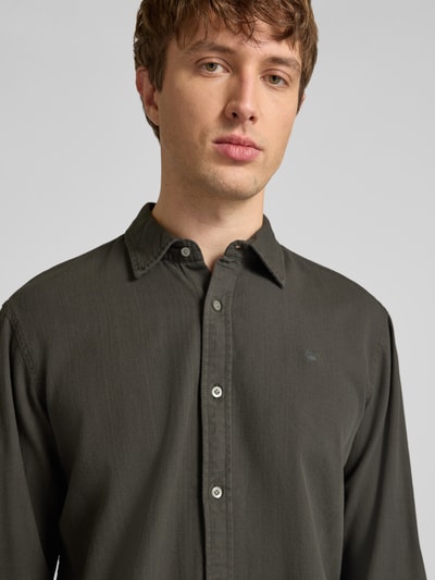 Męski model nosi Regular Fit Freizeithemd aus reiner Baumwolle von G-Star Raw, kolor ciemnoszary, kołnierzyk typu kent, listwa guzikowa, koszula casualowa z bawełny, krój regular fit, długość tyłu w rozmiarze M: 74 cm, szerokość ramion w rozmiarze M: 45 cm, długość rękawów w rozmiarze M: 67 cm, zbliżenie na górną część tułowia
