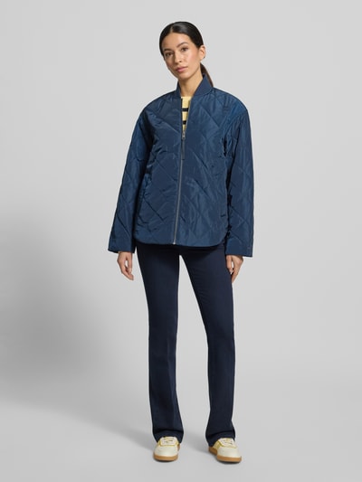 Modelka nosi Regular Fit Bomberjacke mit College-Kragen od Tommy Hilfiger, jednolity kolor, krój regular fit, kołnierz college, długi rękaw, lekko zaokrąglone wykończenie, wodoodporność, boczne kieszenie, logo i aplikacja marki, widok całej sylwetki z przodu.