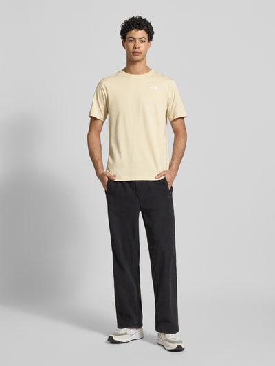Männermodel trägt Regular Fit T-Shirt aus Baumwoll-Mix Modell 'EVOLUTION' von The North Face in Beige mit Label-Detail, Ganzkörperansicht von vorne.