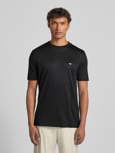 Männermodel trägt T-Shirt mit Label-Stitching von Emporio Armani, schwarz, Lyocell-Baumwoll-Mix, Regular Fit, gerippter Rundhalsausschnitt, Ganzkörperansicht von vorne.