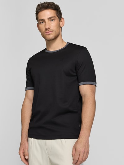 Męski model nosi T-Shirt mit Rundhalsausschnitt od bugatti, czarny kolor, bawełniany miks, krój regular fit, szczegół z logo, długość tyłu w rozmiarze M: 70 cm, zdjęcie całej sylwetki z przodu.