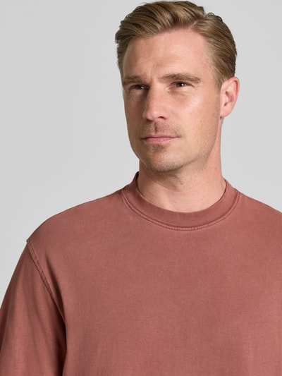 Männermodel trägt Boxy Fit T-Shirt aus reiner Baumwolle Modell 'CORY' von Selected Homme in matt-rostigem Rot, Nahaufnahme Oberkörper.