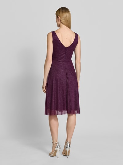 Frauenmodel trägt knielanges Cocktailkleid mit V-Ausschnitt von TROYDEN COLLECTION aus violettem Chiffon mit Glitzer, taillierter Schnitt, breite Träger, rückseitiger V-Ausschnitt und Rückenreißverschluss, Ganzkörperansicht Rückansicht. Kontext: Rückenlänge bei Größe 36: 85 cm, Brustweite bei Größe 36: 43 cm.