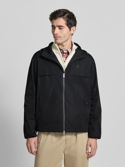 Männermodel trägt Regular Fit Regenjacke mit Logo-Stitching von Polo Ralph Lauren in Schwarz, Kapuze mit Tunnelzug, Zweiwege-Reißverschluss, seitliche Eingrifftaschen, Optik: Unifarben, Ganzkörperansicht von vorne.