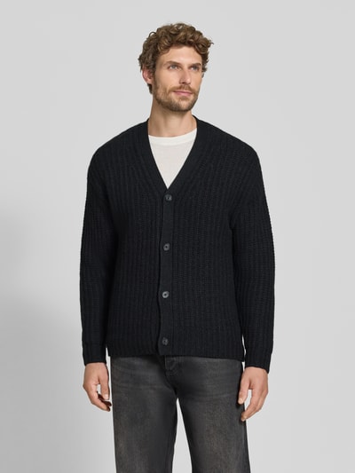 Männermodel trägt Cardigan aus Kaschmir-Mix mit V-Ausschnitt von FTC Cashmere, gerader Schnitt, dunkle Farbe, Nahaufnahme Oberkörper.