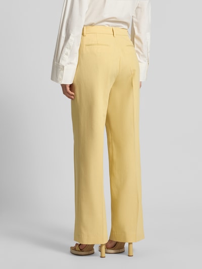 Frauenmodel trägt Wide Fit Stoffhose aus Lyocell-Mix Modell 'Edie' von Scotch & Soda in Gelb mit Bügelfalten, Rückansicht Ganzkörperansicht.