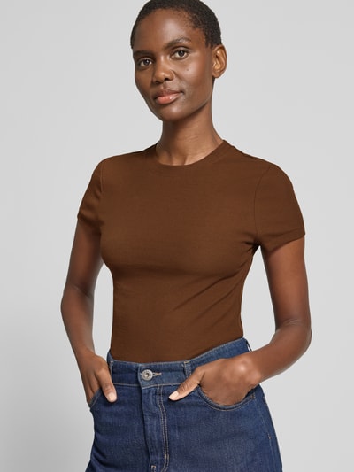 Kobiece model nosi Cropped T-Shirt mit Rundhalsausschnitt od Stefanel, damski t-shirt z mieszanka bawełny, z dodatkiem streczu, krój slim fit, krój krótki, drobne prążkowanie, okrągły dekolt, długość tyłu w rozmiarze S: 53 cm, barwa brązowa; widok na górną część ciała z przodu.