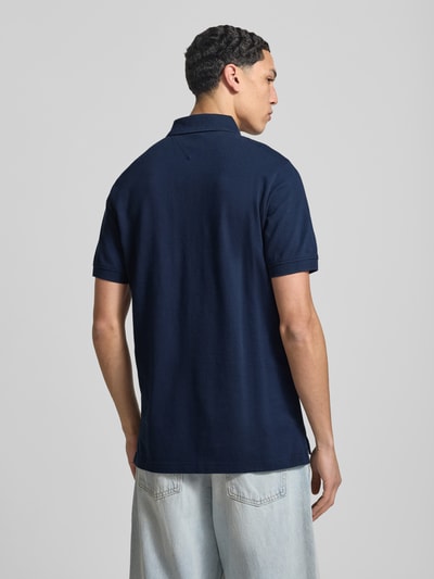 Męski model nosi Regular Fit Poloshirt aus reiner Baumwolle von Tommy Jeans, efekt: jednolity kolor, pika, krótki rękaw, kołnierzyk polo, wyhaftowane logo, kolor granatowy, widok całej sylwetki od tyłu.
