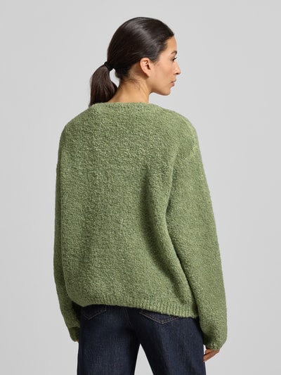 Frauenmodel trägt Strickjacke mit Knopfleiste Modell 'ZOLLY' von American Vintage in Hellgrün, lockerer Schnitt, Lanawoll- und Alpakamix, gerippte Abschlüsse, Rundhalsausschnitt, Rückenlänge 62 cm, Ärmel 70 cm, Ganzkörperansicht Rückansicht.