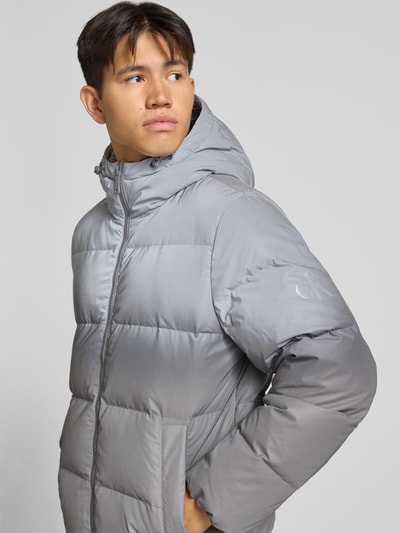 Männermodel trägt Regular Fit Daunenjacke mit Zweiwege-Reißverschluss Modell 'BERKELY' von Calvin Klein Jeans in Hellgrau, Ganzkörperansicht von vorne. Herren Daunenjacke von Calvin Klein Jeans
