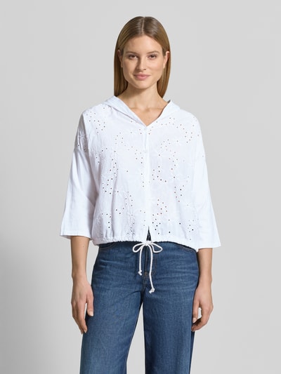 Frauenmodel trägt Bluse mit Kapuze Modell 'Is4aa' von ZABAIONE aus Reine Baumwolle mit Lochstickerei, Gerader-Schnitt, V-Ausschnitt, Knopfleiste, Saum mit Kordelzug, Rückenlänge 53 cm, Ärmellänge 33 cm, in Weiß mit sichtbaren Texturen, Ganzkörperansicht von vorne.