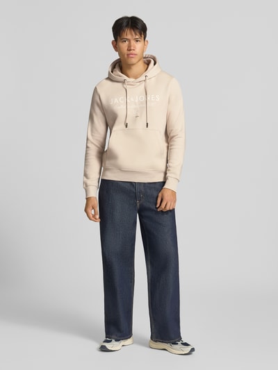 Männermodel trägt Relaxed Fit Hoodie aus Baumwoll-Mix Modell 'KYLE' von JACK & JONES in Beige mit Kapuze, Känguru-Tasche, Ganzkörperansicht von vorne.