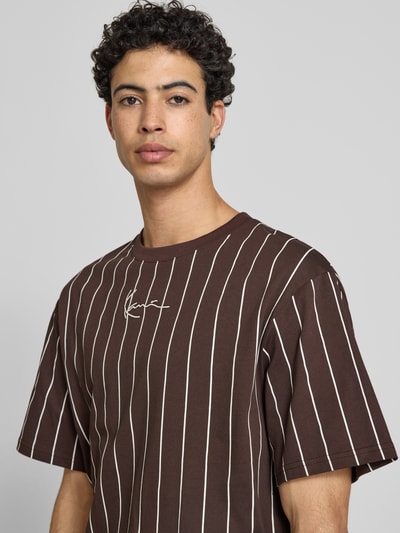 Männermodel trägt Regular Fit T-Shirt mit Logo-Stitching von KARL KANI, braun mit weißen Streifen, Reine Baumwolle, Nahaufnahme Oberkörper. Herren T-Shirt, Rundhalsausschnitt, Rückenlänge bei Größe M: 85 cm.