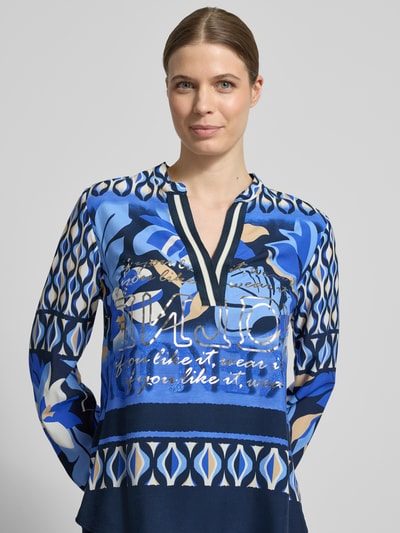 Vrouwenmodel draagt Blusenshirt aus Viskose mit Tunikakragen van Betty Barclay in blauw all-over look met regular fit, zuiver viscose, tuniekkraag en V-hals, ruglengte maat 36: 67 cm, mouwlengte maat 36: 65 cm. Nahaufnahme bovenlichaam.