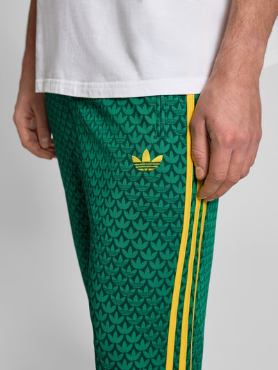 Männermodel trägt grüne Sweatpants mit gelbem Label-Stitching von adidas Originals, seitliche gelbe Streifen, Nahaufnahme Oberschenkel.