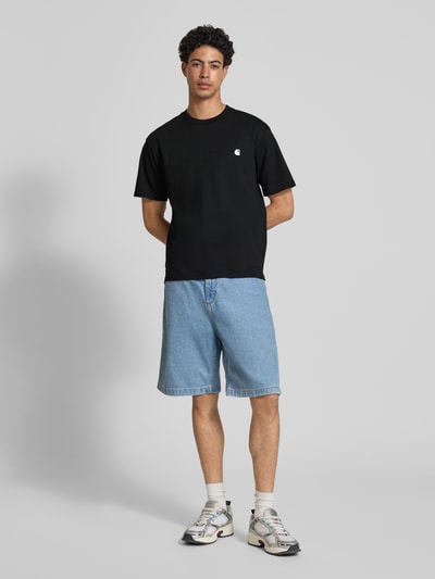 Männermodel trägt Herren T-Shirt mit Label-Stitching Modell 'Madison' von Carhartt Work In Progress aus Reine Baumwolle, Regular-Fit, schwarz, Rundhalsausschnitt, Rückenlänge bei Größe M 75 cm, Ganzkörperansicht von vorne.