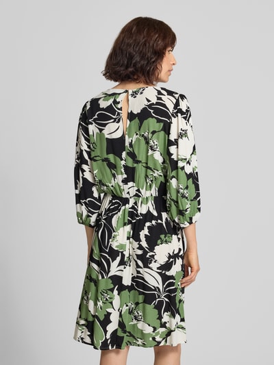 Frauenmodel trägt knielanges Kleid aus Viskose im Allover-Look Modell 'Fe44li' von ZABAIONE mit grün-schwarzem Blumenmuster, Ganzkörperansicht Rückansicht. Damen Kleid, reine Viskose, A-Linie, V-Ausschnitt, 3/4-Arm, Rückenlänge 98 cm, Brustweite 52 cm, Ärmellänge 46 cm.