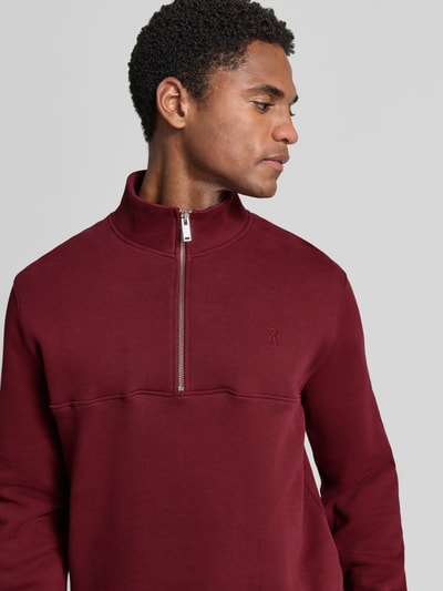 Männermodel trägt Regular Fit Troyer aus reiner Baumwolle Modell 'WAARLO' von ARMEDANGELS in Dunkelrot, Nahaufnahme Oberkörper.