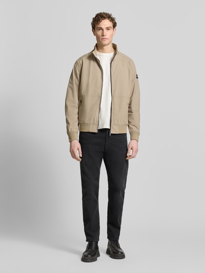 Męski model nosi Regular Fit Jacke mit Stehkragen od Lerros, beżowa, elastyczny materiał, zamek, kieszenie na zamek, logo, pełny widok z przodu. Szerokość w rozmiarze M: 58 cm, długość tyłu: 67 cm, szerokość ramion: 49 cm, długość rękawa: 68 cm.