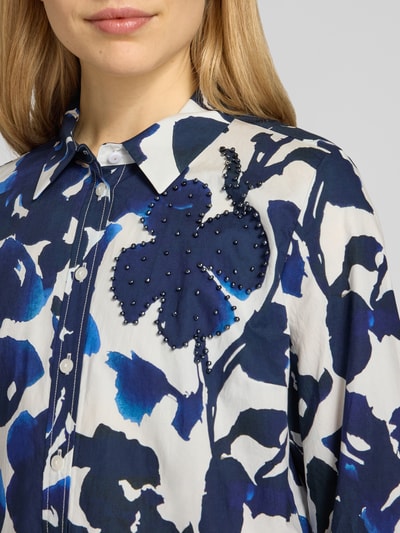 Frauenmodel trägt knielanges Hemdblusenkleid im Allover-Look von WHITE LABEL aus reiner Baumwolle, blaue Muster, Perlen, Nahaufnahme Oberkörper.
