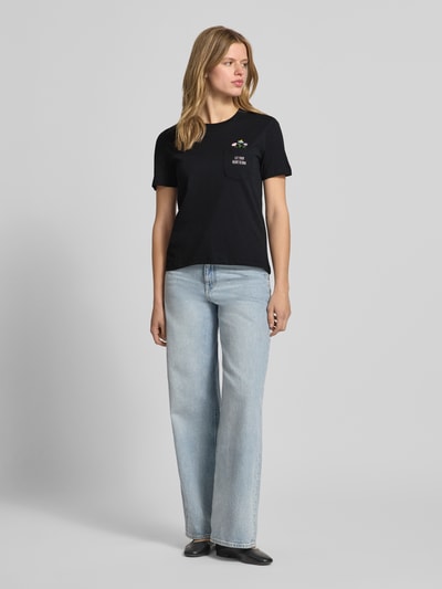 Frauenmodel trägt Regular Fit T-Shirt aus reiner Baumwolle Modell 'POLLY' von Only, schwarz, unifarben mit Stickerei, Rundhals, Brusttasche, Kurzarm, Ganzkörperansicht von vorne