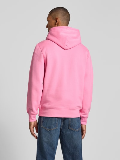Männermodel trägt Regular Fit Hoodie aus Baumwoll-Mix von Tommy Hilfiger in Rosa, kombiniert mit blauer Jeans, Ganzkörperansicht Rückansicht.