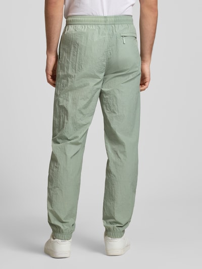 Männermodel trägt Straight Fit Stoffhose mit Logo-Stitching Modell 'Nayla' von SERGIO TACCHINI in Hellgrün, elastischer Bund mit Tunnelzug, elastische Beinabschlüsse, Struktur in Anzug-Stoff:, Innenbeinlänge 77 cm bei Größe M, Ganzkörperansicht Rückansicht.
