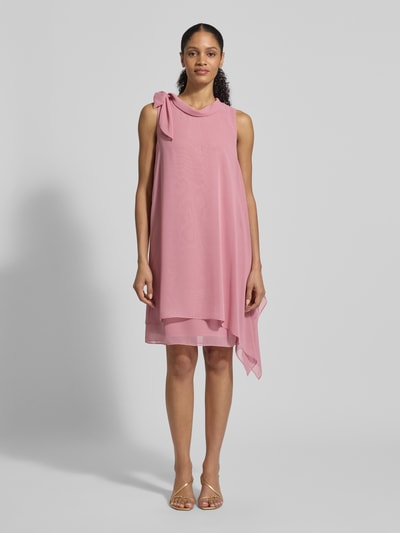 Modelka prezentuje Relaxed Fit Kleid mit Stehkragen od Vera Mont w kolorze pudrowego różu, półprzezroczysty materiał z widoczną podszewką, ozdobna kokarda, bez rękawów, długość tyłu w rozmiarze 36 to 98 cm, szerokość w rozmiarze 36 to 29 cm, widoczne delikatne tekstury, całkowity widok z przodu.