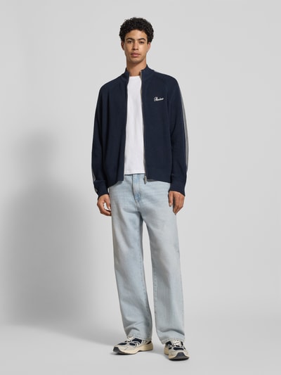 Männermodel trägt Regular Fit Jacke in Strick-Optik von REVIEW, dunkelblau mit Kontraststreifen und Logo-Stitching, Ganzkörperansicht von vorne, reine Baumwolle, Stehkragen, Reißverschluss, elastische Abschlüsse, Rückenlänge 67 cm, Ärmellänge 73 cm.