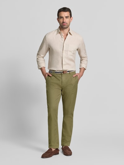 Männermodel trägt Chino mit Gürtel und Eingrifftaschen Modell 'WARREN' von Scotch & Soda in Olivgrün, Baumwoll-Mix, Ganzkörperansicht von vorne.