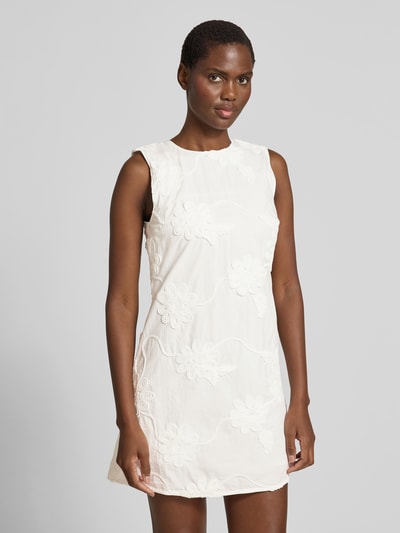 Frauenmodel trägt Minikleid mit floralem Zierbesatz von ROTATE aus weißer Baumwolle, leicht taillierte Passform, Nahaufnahme Oberkörper.