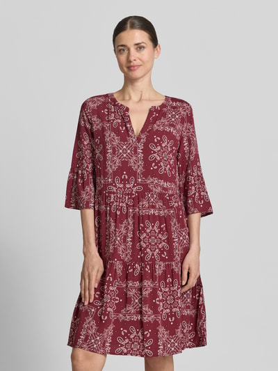 Frauenmodel trägt Relaxed Fit Minikleid aus reiner Viskose mit Allover-Paisley-Print von Christian Berg Woman Selection, Tunika-Ausschnitt, 3/4-Arm, in Weinrot mit weißen Mustern, glatte Textur, Ganzkörperansicht von vorne.