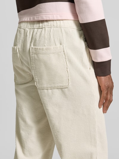Männermodel trägt Straight Fit Cordhose aus reiner Baumwolle Modell 'Padow' von American Vintage, cremefarben, samtartige Struktur, Gesäßtaschen, elastischer Bund, Ganzkörperansicht Rückansicht.