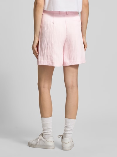 Modelka nosi szorty z tyłu kieszeń z wypustką model 'EMMA' od JJXX, krój loose fit, kolor jasnoróżowy, długość wewnętrzna nogawki 14 cm, szerokość w rozmiarze S 37 cm, zapięcie na haftkę i zamek błyskawiczny, wpuszczane kieszenie z przodu, widok całej sylwetki z tyłu.