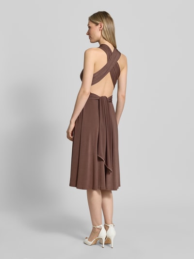 Frauenmodel trägt knielanges Cocktailkleid mit tiefem V-Ausschnitt von Rose Avenue in Braun, taillierter Schnitt, mit Taillenband, Rückseite gekreuzte Träger, glatte Textur, Rückenlänge bei Größe S 44 cm, Ganzkörperansicht Rückansicht.