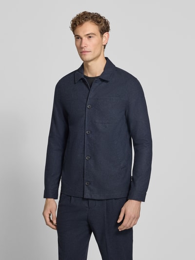 Męski model nosi Regular Fit Jacke mit Woll-Anteil von Lindbergh, elastyczna mieszanka materiałów, wykładany kołnierz, kieszeń na piersi, listwa guzikowa, kolor granatowy, długość tyłu w rozmiarze M: 72 cm, widok całej sylwetki z przodu.