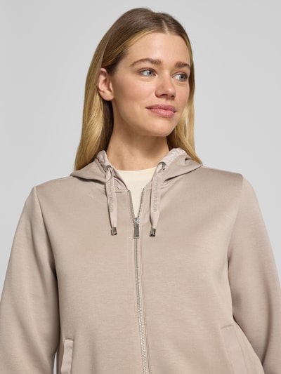 Modelka nosi Regular Fit Sweatjacke mit Viskose-Anteil od Tom Tailor, efekt: jednolity kolor, krój regular fit, zamek błyskawiczny, z napisem z logo, kaptur z tunelkiem, okrągły dekolt, długi rękaw, zakończenia rękawów prążkowane, boki z rozcięciami, wpuszczane kieszenie, wykończenie materiału: dzianina dresowa, materiał: mieszanka materiałów z dodatkiem wiskozy, zbliżenie na górną część ciała